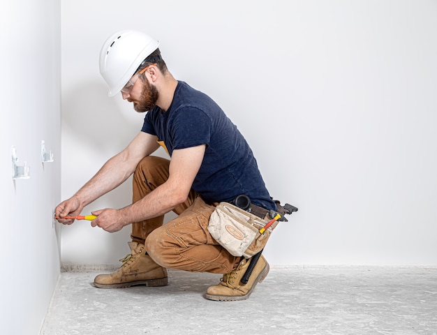 Professioneel in overall met een elektriciensgereedschap op de witte muurachtergrond.