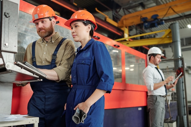 Foto professioneel van industriële installaties functie van cnc-machine uit te leggen aan aziatische werknemer in werkplaats