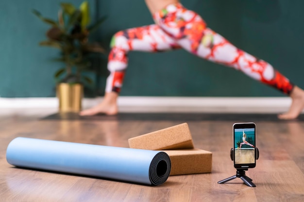 Professioneel yoga-trainingsstatief met telefoon en matrol op de vloer tegen vrouw die in pose staat