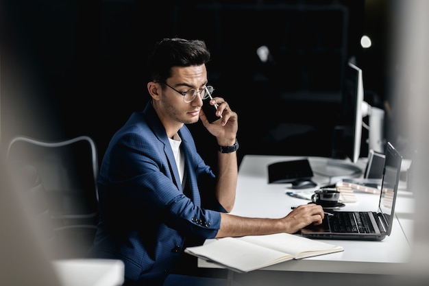 Professionele architect gekleed in een pak praten via de telefoon en werkt op de laptop op kantoor.