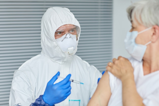 Professionele arts die handschoenen draagt die antivirale injectie geven aan oude vrouw die voor hem in ziekenhuisafdeling zit