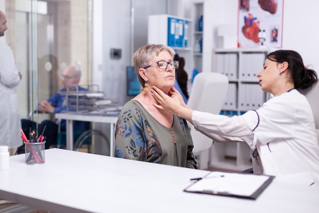 Professionele arts die neklymfeklieren van oude vrouw controleert, senior vrouw palperend. Oudere patiënt die een arts bezoekt in het ziekenhuis die de schildklierkeel onderzoekt en de gezondheid in de kliniek aanraakt, medische behandeling