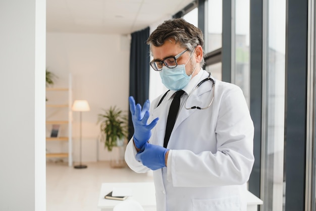 Professionele arts met medisch masker die handschoenen aantrekt Zelfverzekerde arts in laboratoriumjas die bescherming draagt tijdens de uitbraak van covid19 Preventie van virale ziekten