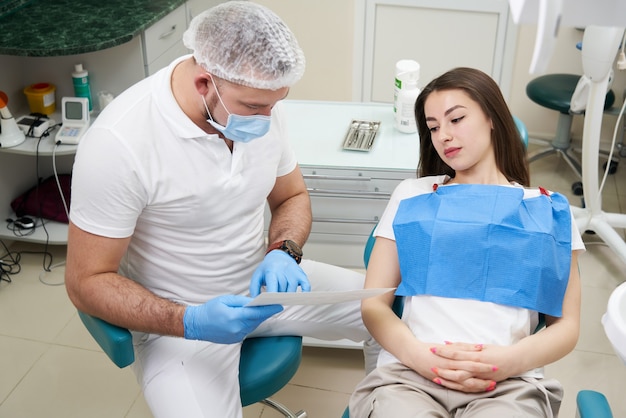 Professionele arts toont aan de patiënt foto van tanden in zijn medische tandheelkundige kantoor. Arts die medische kleding draagt.