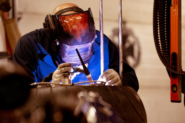 Foto professionele automonteur die in de autoreparatiedienst aan de snijmachine van het argongas werkt