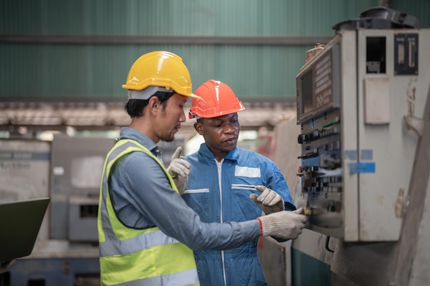 Professionele aziatische arbeider en afrikaanse man staan en onderhouden de grote machine in de fabriek