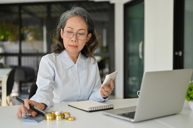 Professionele Aziatische senior vrouwelijke accountant die het budget beheert met behulp van een rekenmachine