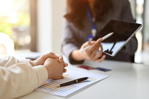 Professionele Aziatische vrouwelijke bankier die iets op het tabletscherm laat zien aan haar cliënt