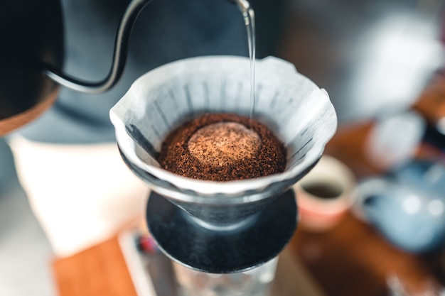 Professionele barista die koffie bereidt, giet over koffiezetapparaat en druppelketel