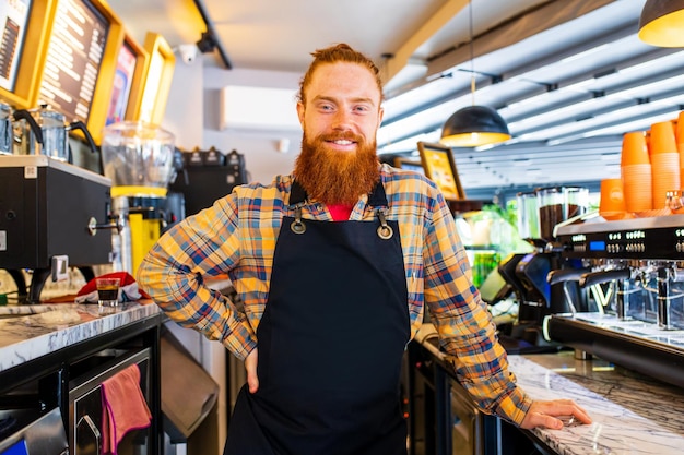 Foto professionele barista jonge roodharige gember bebaarde man in zwarte schort werken in coffeeshop