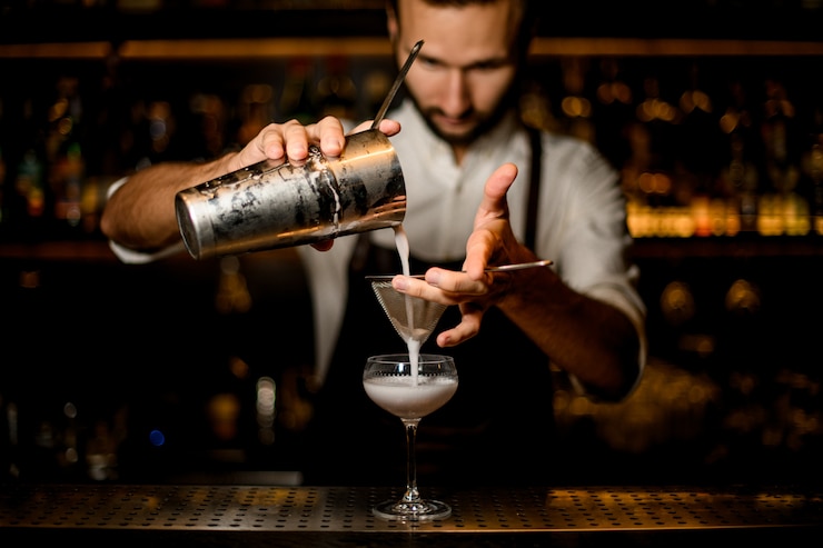 Foto professionele barman gieten een witte cocktail van de stalen shaker naar het glas door de zeef