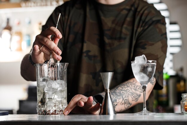 Professionele barman roert koude cocktail met lepel Verschillende flessen alcoholische dranken en glazen staan op de toog