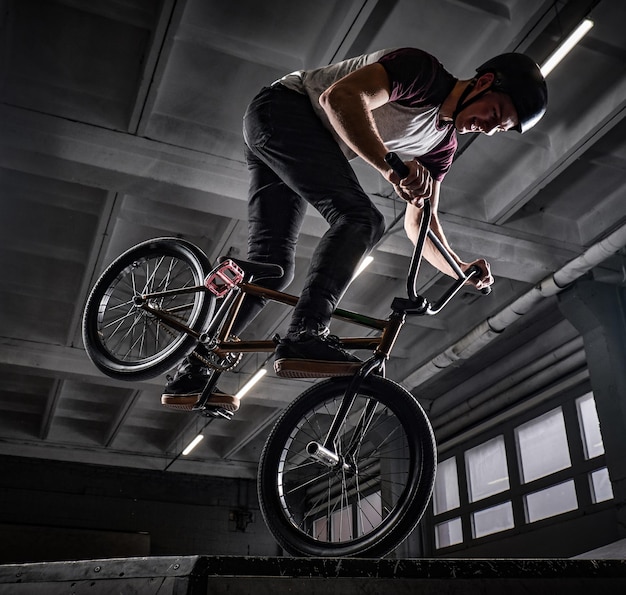 Professionele BMX-rijder in beschermende helm die trucs uitvoert in skatepark binnenshuis