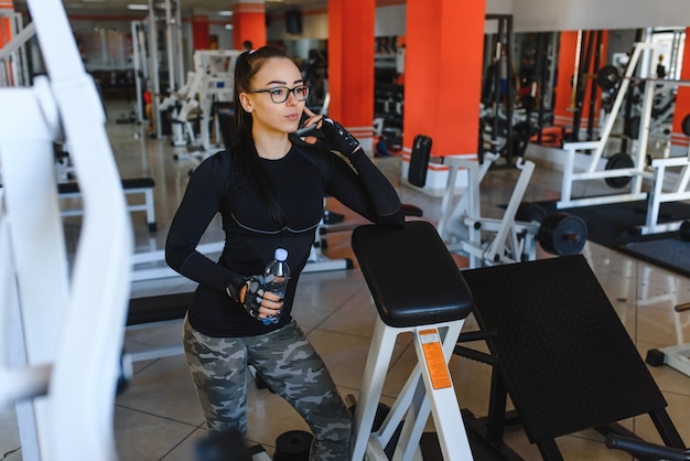 Professionele bodybuilding-atleet ontspannen na een vermoeiende training. Atleet ontspannen en water drinken uit sportfles in sportschool interieur.