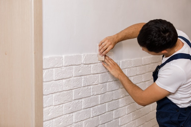 Professionele bouwer die decoratieve tegels op muur lijmen. werknemer monteert decoratieve baksteen op de muur