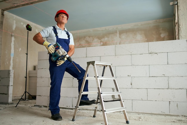 Professionele bouwvakker in uniform staande met boorhamer portret van aannemer