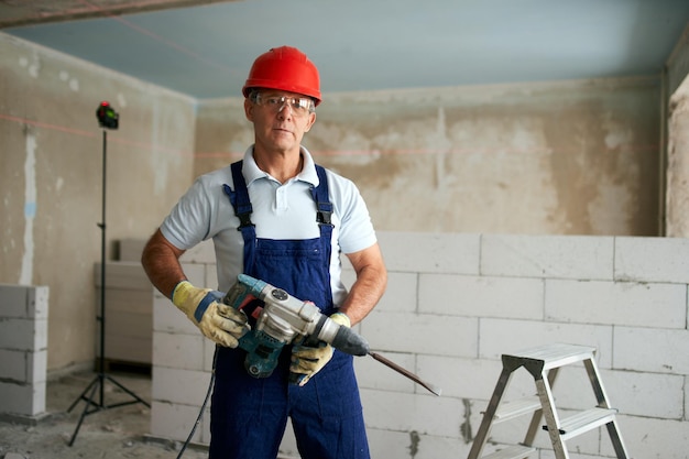 Professionele bouwvakker in uniform staande met boorhamer portret van aannemer