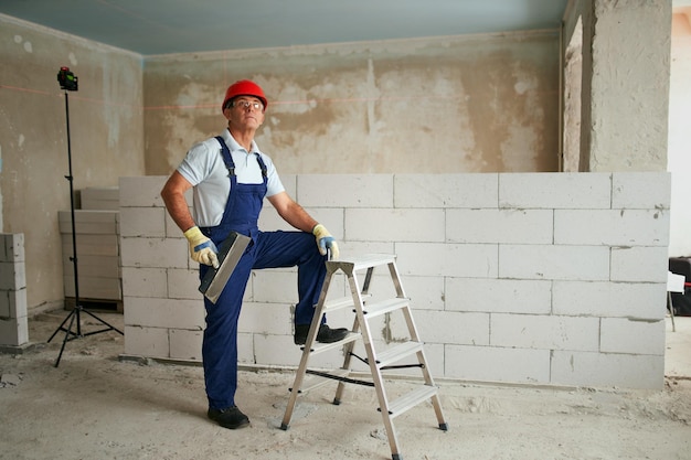 Professionele bouwvakker in uniform staande met spatel op stap ladder portret van