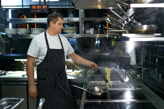 Professionele chef-kok die vegetarische Italiaanse pasta maakt op een modern keukengasfornuis in een wokpan