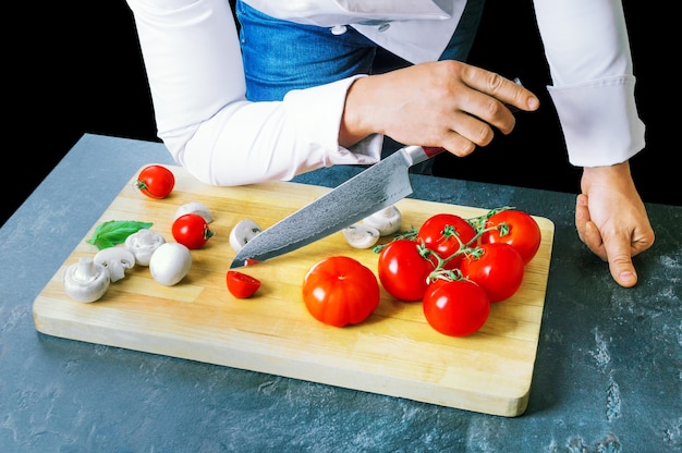 Professionele chef-kok snijdt groenten met een scherp mes van damascus-staal. gemengde media