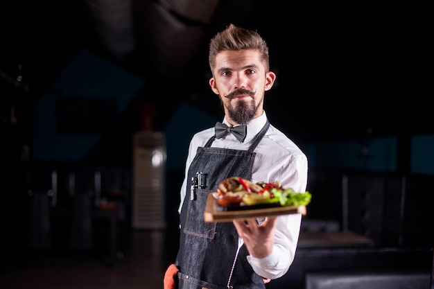 Professionele flunkey biedt bezoekersbord met bereid gerecht op een zwarte achtergrond.