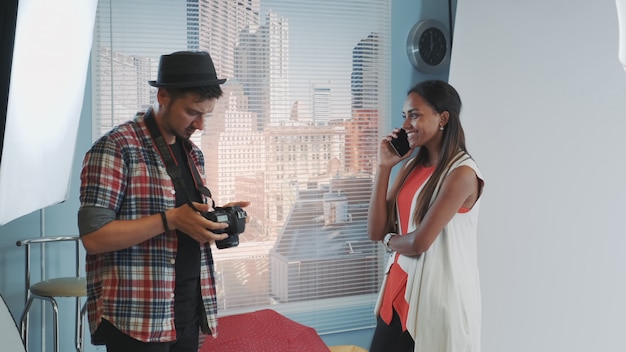 Professionele fotograaf die zijn camera controleert en het model spreken op de telefoon