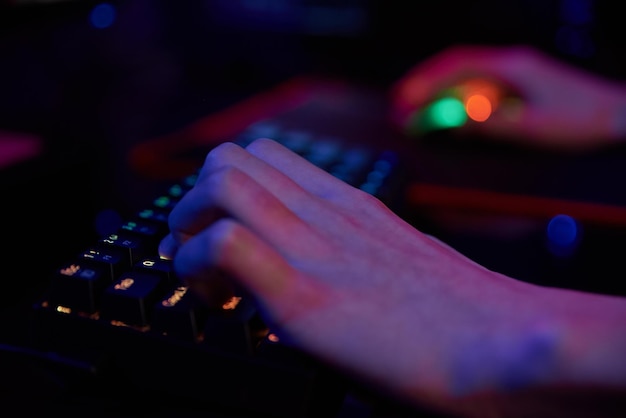 Professionele gamer speelt computervideogame in een donkere kamer en gebruikt een neonkleurige rgb mechanische toetsenbordplaats voor cybersport-gaming