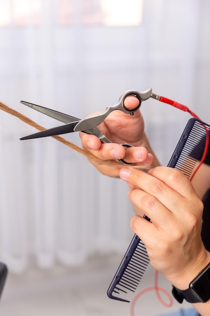 Professionele haarstylist met kam en hete thermische schaar snijpunten van lang steil haar slot close-up