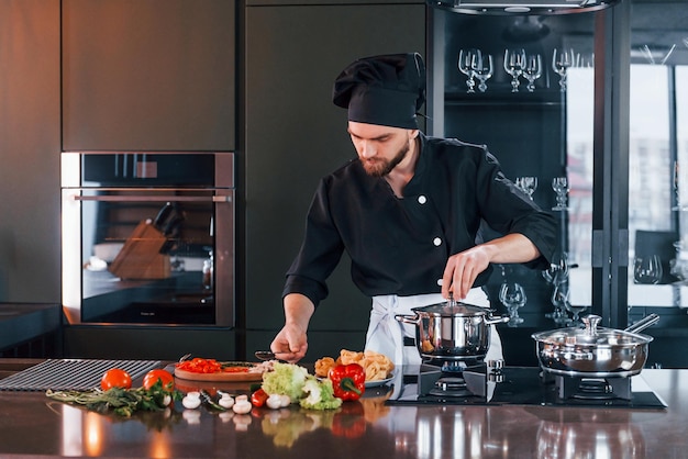 Professionele jonge chef-kok in uniform die aan de keuken werkt