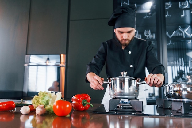 Professionele jonge chef-kok in uniform heeft een drukke dag in de keuken
