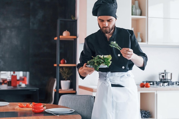Professionele jonge chef-kok in uniform salade maken in de keuken