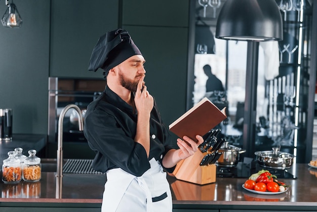 Professionele jonge chef-kok in uniform staande met notitieblok op de keuken