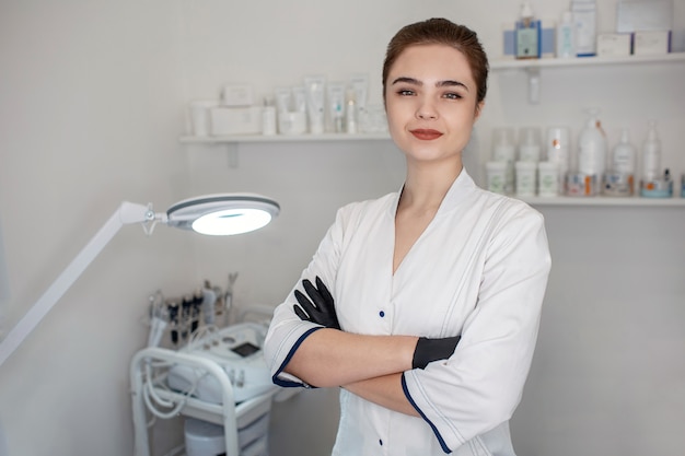 Foto professionele jonge schoonheidsspecialiste staan in de cosmetologie kamer en pose. ze hield gekruiste benen. model ziet er zelfverzekerd uit.