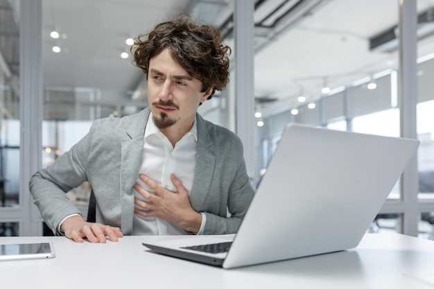 Professionele jonge volwassen mannelijke kantoorwerker die ongemakkelijk of gestrest lijkt met zijn hand op de borst