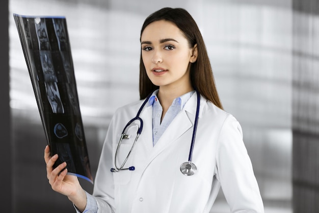 Foto professionele jonge vrouwelijke arts kijkt naar het röntgenogram van haar patiënt arts aan het werk in het kantoor van een kliniek geneeskundeconcept