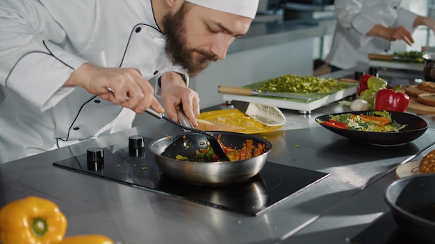 Professionele kok bereidt een culinair recept met groenten voor, met behulp van een koekenpan op het fornuis om een verse gastronomische maaltijd te maken. Mannelijke chef-kok koken gastronomisch gerecht in authentieke keuken. Detailopname.