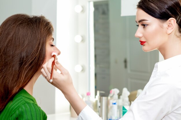 Professionele make-up artiest poeder met blos toe te passen op de wangen voor jonge mooie vrouw in schoonheid
