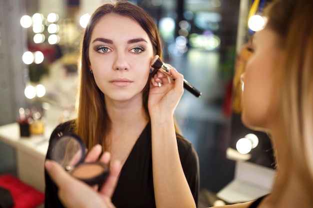 Professionele make-up artiest werken met mooie jonge vrouw. Modieuze vrouw