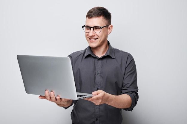 Professionele man met een bril die een laptop gebruikt op een grijze achtergrond met een gefocuste uitdrukking