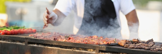 Professionele mannelijke chef-kok die vers vlees op grill op open lucht frituurt