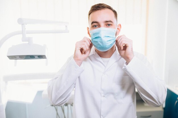 Professionele mannelijke tandarts die een medisch masker opzet en zich klaarmaakt voor werk