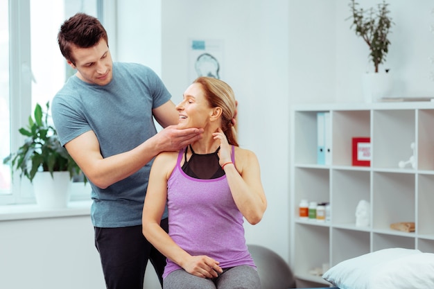 Professionele masseur. Aangename sterke man die achter zijn patiënt staat terwijl hij een massage voor haar doet