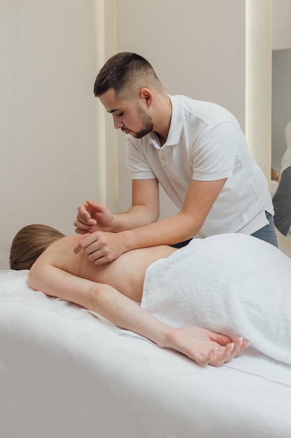 Professionele masseur maakt corrigerende lichaamsmassage aan het lichaam van een vrouw die met haar gezicht naar beneden op de massagetafel ligt in de spa salon