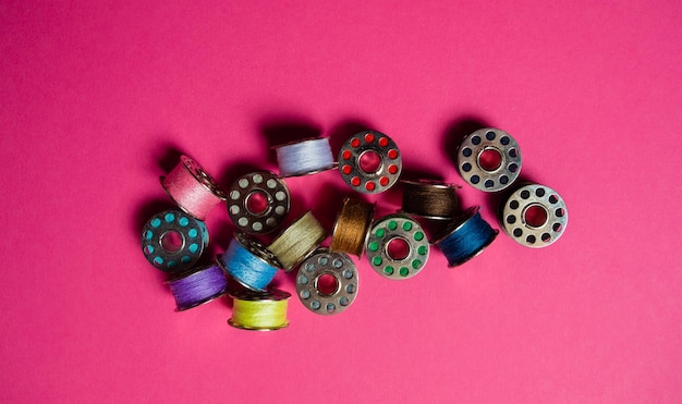 Professionele metalen naaimachineklossen met kleurrijke draden Verbruiksartikelen voor naaimachine boven het hoofd op roze oppervlak