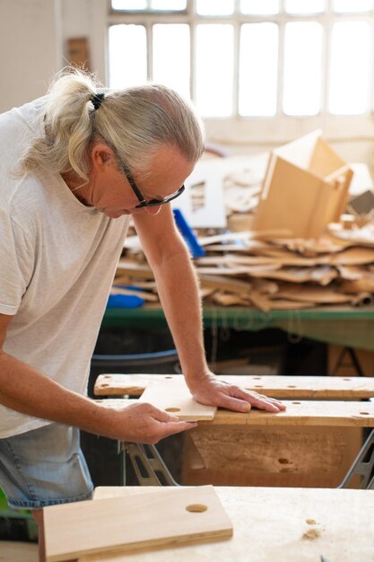 Foto professionele oudere timmerman die in de werkplaats met timmerwerktuigen aan hout werkt