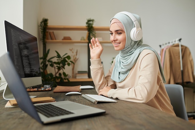 Professionele programmeur uit het Midden-Oosten die hijab en koptelefoon draagt en deelneemt aan onlinevergaderingen