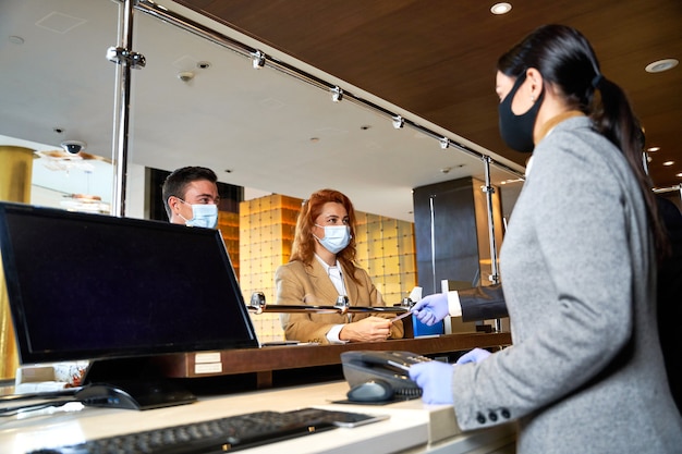 Professionele receptionisten en hotelgasten die de veiligheidsmaatregelen in acht nemen en communiceren in medische maskers