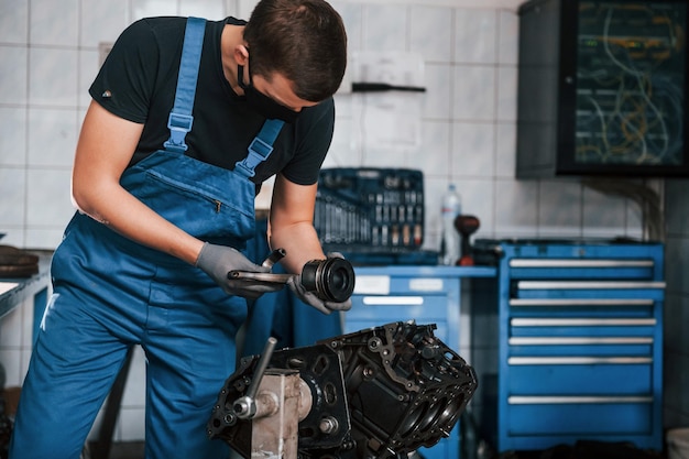 Professionele reparateur in zwart beschermend masker werkt met kapotte automotor