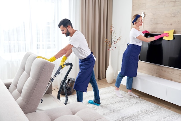 Professionele schoonmakers in blauw uniform wassen vloer en stof van het meubilair in de woonkamer van het appartement vegen. Schoonmaak dienstverleningsconcept