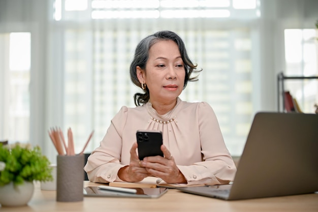 Professionele senior Aziatische zakenvrouw aan haar bureau die naar het scherm van de laptop kijkt